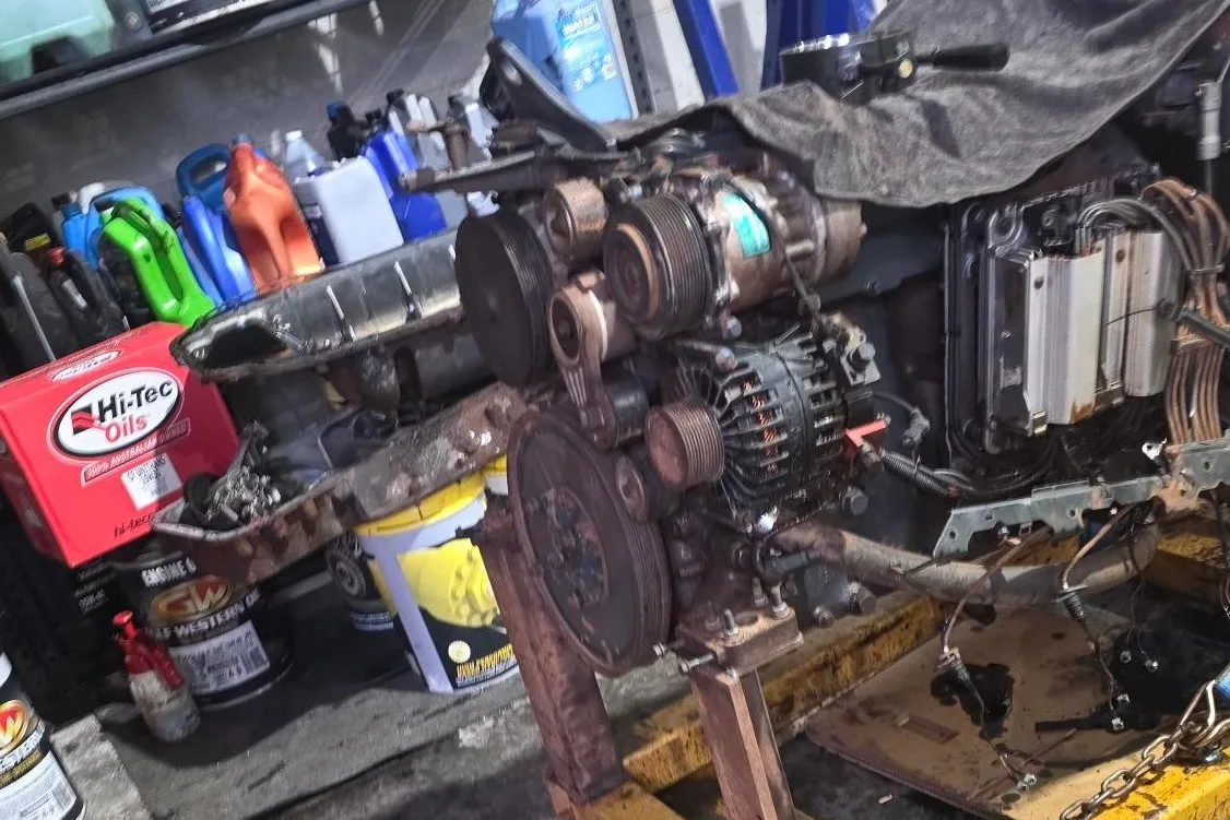 A diesel engine on a stand in the workshop with the sump off and the belts, pulleys and alternator exposed