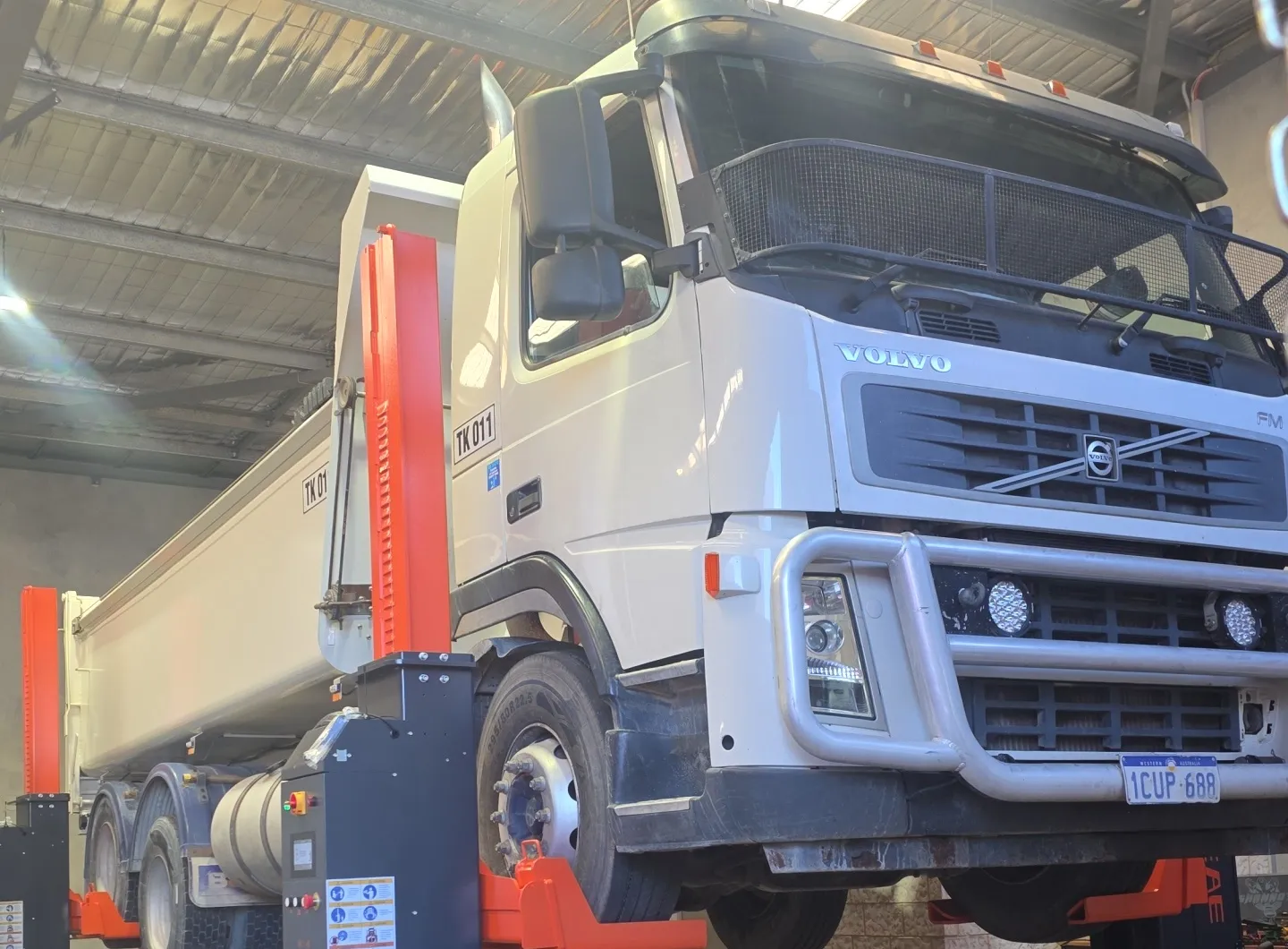 A white Volvo tipper raised on orange mobile column lifts in the workshop